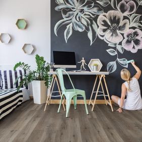 Kvinne sitter på gulv i stue og tegner på vegg